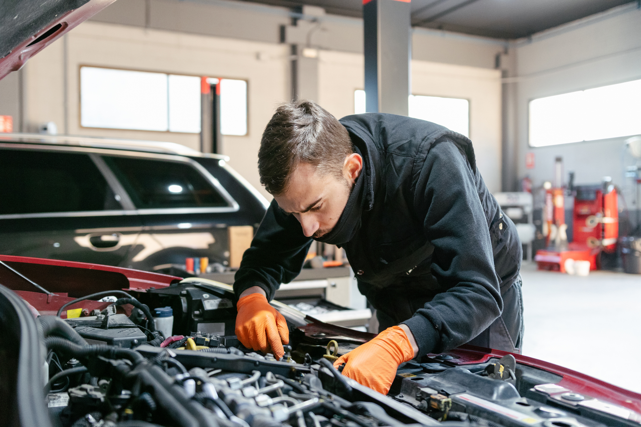 Car mechanic working on a vehicle in a well-equipped garage. Wearing a uniform and using tools, he focuses on fixing the car to ensure it runs smoothly